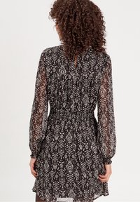 Robe noire à motifs avec une taille cintrée, des manches longues bouffantes et un dos avec ouverture en forme de goutte, réalisée en tissu léger et transparent.