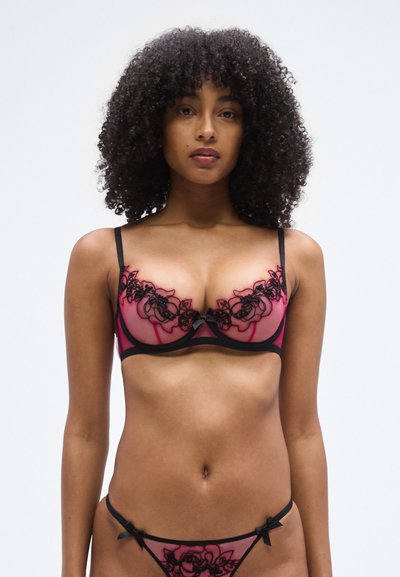 Lace-trimmed pink and black lingerie set featuring a bra with sheer cups and floral embroidery, complemented by a matching thong with bow accents.