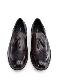 Zapatos de piel marrón oscuro con un acabado suave, detalles perforados, acentos tipo brogue y borlas decorativas. Diseñados como mocasines.
