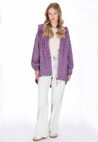 Lila leopárdmintás dzseki kapucnival, cipzáras záródással és rugalmas mandzsettákkal. Világos farmer flare nadrággal és fehér tornacipővel párosítva.