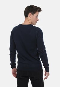 Pull en tricot bleu marine avec manches longues, col rond et poignets côtelés. Texture lisse avec une coupe ajustée, montré de dos.