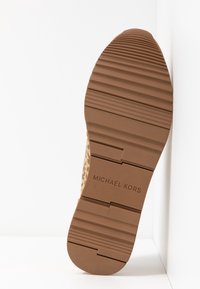 Suola in gomma marrone con superficie testurizzata e scanalature. Presenta "MICHAEL KORS" impresso su una sezione a motivo. Design atletico classico.