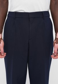 Pantaloni tailored, de culoare navy, dintr-un material texturat. Prezintă plii în față, bucle pentru curea și un talie netedă. Design curat, fără embellishments.