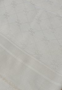 Tessuto color crema con un sottile motivo di fiori stilizzati, caratterizzato da delicate trame e sottili righe intrecciate lungo i bordi.