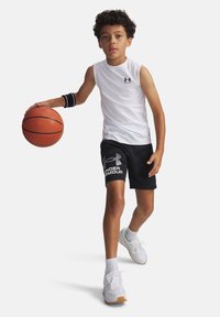Biele bezrukávové športové tričko, čierne šortky s logom, čierny návlek na ruku, drží basketbalovú loptu, obuté biele tenisky s textúrovanými podrážkami.