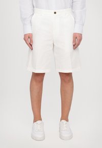 Hvite linshorts med avslappet passform, med flat front, sidelommer og diskrete sømmer. Kombinert med hvite joggesko.