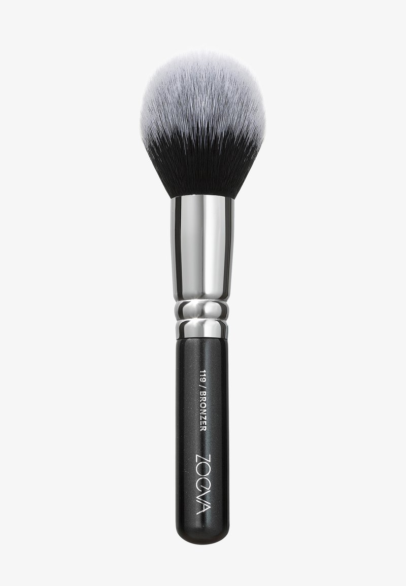 Pennello per trucco con una testa di setole densa e arrotondata in bianco e nero, un elegante ferretto in argento e un manico nero opaco con testo inciso.