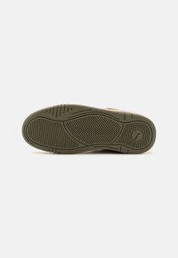 Suola di sneaker in gomma verde oliva, caratterizzata da un design testurizzato con scanalature diagonali e orizzontali per una migliore aderenza, e un logo circolare.