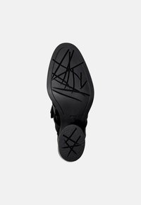 Suela de calzado negra con patrones de agarre texturizados, presentando una superficie lisa y un diseño en forma de onda a lo largo de los bordes.