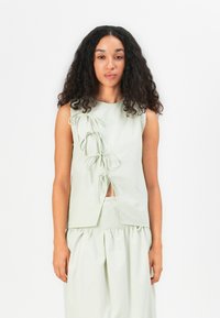 Top senza maniche verde chiaro con fiocchi laterali e uno spacco frontale, realizzato in tessuto morbido, che presenta una vestibilità comoda e una texture liscia.