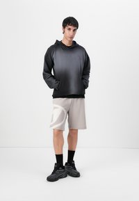 Hanorac cu glugă din material negru cu gradient, cu mâneci lungi, asociat cu pantaloni scurți bej cu un model abstract mare, de culoare deschisă.