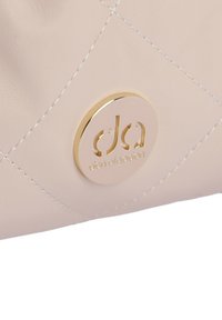 Bolso de mano de piel acolchada beige que presenta un logo dorado redondo con el texto "dan algadjan", detalles de costura sutiles y una textura suave.