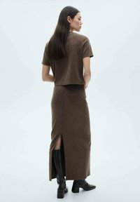 Ensemble en tricot marron composé d'un haut court et d'une jupe longue avec une fente latérale, assorti de bottes noires jusqu'aux genoux.