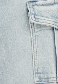 Světle modrá denimo tkanina s přehnutou kapsou, viditelným švem a jemnou texturou, která zdůrazňuje klasický design džínů.