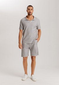 Gestreiftes Poloshirt in Beige und Marineblau mit Kragen, kombiniert mit passenden Shorts. Aus weichem Stoff mit lässigem Schnitt. Weiße Sneaker.