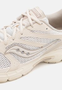 Beige Laufschuh mit einem Mesh-Obermaterial, strukturierten synthetischen Überzügen und einer gepolsterten Sohle. Verfügt über reflektierende Akzente und flache Schnürsenkel.