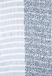 Tissu en coton avec une séparation verticale ; côté gauche avec des rayures horizontales bleu clair, côté droit avec un motif floral bleu dense sur fond blanc.