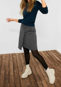 Zwart-wit gestreepte wikkelrok gecombineerd met een marineblauwe trui, zwarte maillots en crèmekleurige enkellaarsjes. Achtergrond van houten planken.