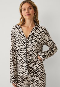 Leopardprint natdragt i beige med sorte pletter. Lange ærmer, knaplukning foran og brystlomme. Blødt stof med en afslappet pasform.