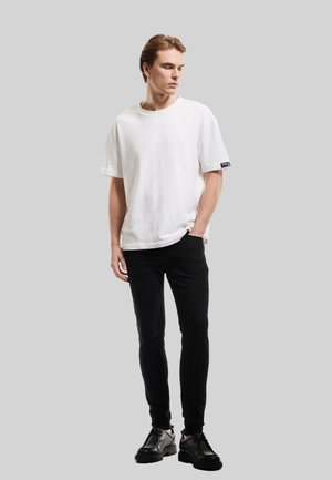 Biała bawełniana koszulka z krótkimi rękawami, okrągłym dekoltem, zestawiona z czarnymi slim-fit spodniami i czarnymi butami. Prosty design, minimalna marka.