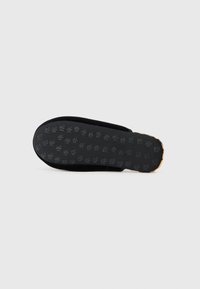 Suela de zapato negra con patrón de goma texturizada, que presenta un borde suave y una ligera curvatura. El material parece duradero y flexible.
