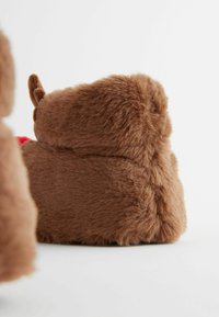 Brun plyschdjurtoffel med mjuk, fluffy textur. Rund form och små öron som detalj. Röda accenter synliga, mot en vit bakgrund.