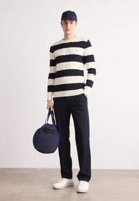 Mėlynas ir kreminės spalvos dryžuotas raštinis megztinis su apykakle, derinamas su mėlynomis kelnėmis. Akcentai: apvalus mėlynas krepšys ir baltos sportbačiai.