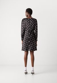 Abito nero a pois con maniche lunghe, vita cinte e gonna svasata. Tessuto liscio, scollatura rotonda e chiusura con bottoni sul retro.