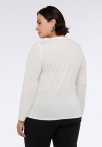 Maglia a maniche lunghe beige chiaro con scollo rotondo, caratterizzata da una leggera texture brillante. Abbinata a jeans neri.