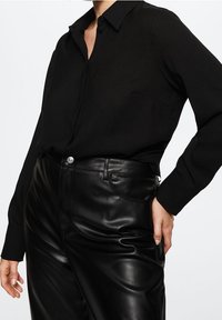 Black button-up shirt with a collar, paired with high-waisted black faux leather pants. Smooth texture, fitted design, and minimal details.