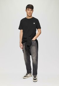 Zwarte T-shirt met korte mouwen en een klein logo op de borst, gecombineerd met donkergrijze spijkerbroeken en meerkleurige sneakers.