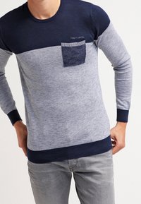 Marineblauer und grauer Pullover mit Blockfarben, Rundhalsausschnitt, gerippten Bündchen und einer Tasche mit gestreiftem Besatz. Hergestellt aus weichem Strickstoff.