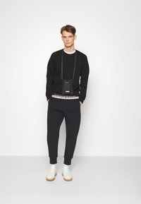 Czarny sweatshirt z długim rękawem, w połączeniu z granatowymi spodniami dresowymi i białymi sneakersami. Mała torebka na ramię wisi na szyi.