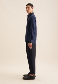 Marineblauw overhemd met knopen en een spitse kraag, lange mouwen en manchetten met één knoop, gecombineerd met zwarte slim-fit broek en nette schoenen.