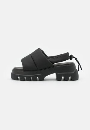 Sorte chunky sandaler med en polstret overdel og åben hæl. Den tykke sål har et mønstret design for greb og stabilitet.