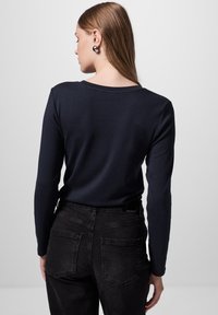 Marineblauw langemouwen top met een ronde halslijn, gedragen met zwart jeans met achterzakken en een subtiele textuur.