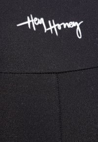 Černé legíny s vroubkovanou texturou, které mají na pase výšivku bílého loga "Hey Honey". Hladký, elastický materiál.