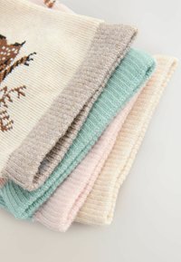 Fire strikkede sweatre stablet. Farverne inkluderer creme, mintgrøn, lys pink og lysebrun, med ribbede teksturer og kontrastkanter.