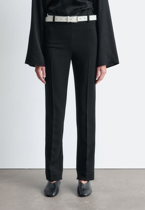 Black tailored pants with a straight fit, made from a smooth fabric. Accented by a white belt and paired with black pointed shoes.