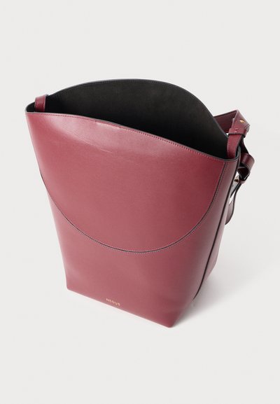 Bolso tote de cuero burdeos con una amplia abertura, parte superior curva y forro interior negro. Cuenta con una correa ajustable y un sutil detalle del logo.