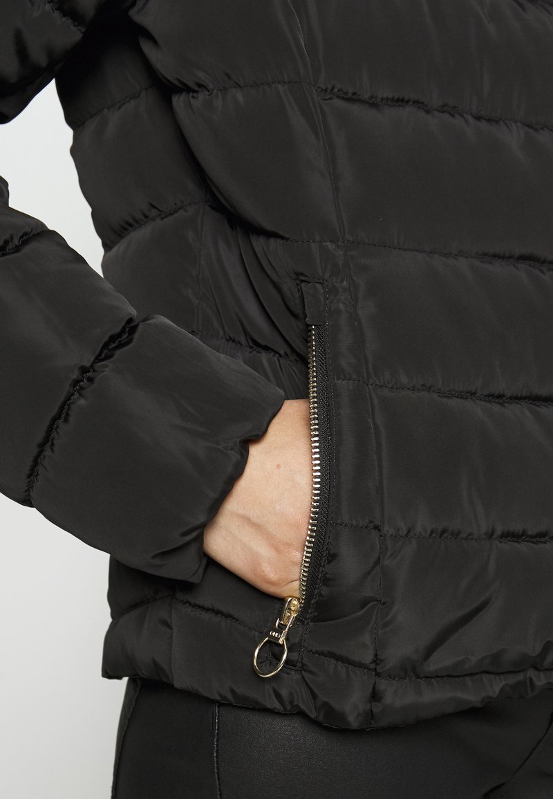 Giubbotto piumino nero con cuciture a righe, tasca con zip, parti in metallo dorato e un tessuto morbido e strutturato.