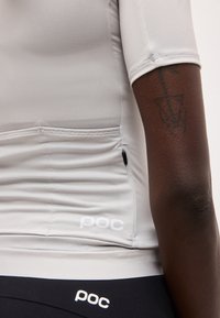 Κοντινό πλάνο ενός ατόμου που φοράει ανοιχτό γκρι ποδηλατική φανέλα με πίσω τσέπες και ένα μαύρο τατουάζ στο δεξί χέρι.