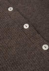 Cardigan en brun texturé avec des côtes verticales et quatre boutons ronds de couleur claire le long de la patte de boutonnage. Matière tricotée douce.