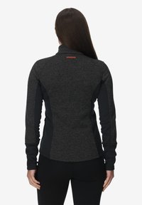 Giacca sportiva grigia e nera con colletto alto, tessuto texture, maniche lunghe e un piccolo logo rosso sulla parte posteriore.