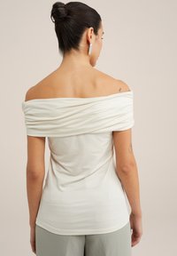Top bianco scollato sulle spalle, drappeggiato e realizzato in un materiale morbido. Design aderente con maniche corte, orlo curvo e tessuto testurizzato.