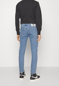 Ljust blå jeans med slim fit, med bakfickor och en vit Calvin Klein-etikett. Bärs med en svart sweatshirt och svarta sneakers.
