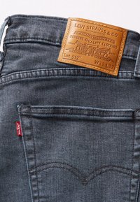 Mörkblå denimjeans med en läderetikett som visar "Levi Strauss & Co." sydd på baksidan, med en röd flik och klassisk fickdesign.