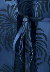 Gros plan d'un tissu bleu à motifs floraux noirs noué en un nœud avec des bretelles à motifs assortis.