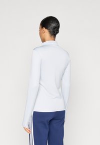 Ανοιχτό μπλε μπλουζάκι με μακριά μανίκια και ψηλό γιακά, με λεία υφή και εφαρμοστή γραμμή, συνδυασμένο με σκούρο μπλε παντελόνι με λευκές ρίγες.