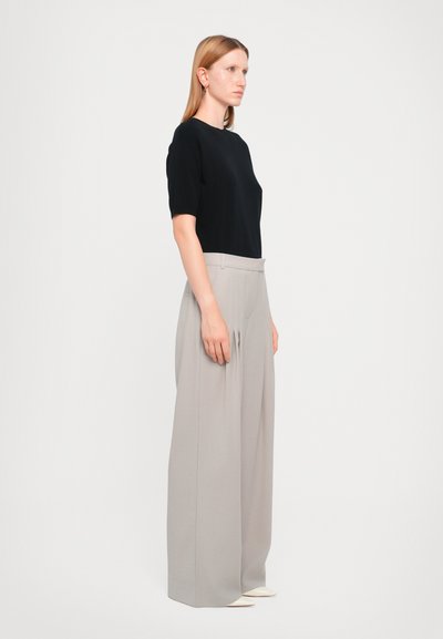 Zwart kortemouwen T-shirt gecombineerd met hoge taille, lichtgrijze wijde broek. De broek heeft voorplooien en een soepele, lichte stof.